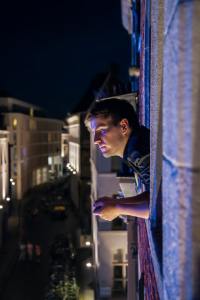 man leaning on frame of window with head sticking out high over a city
