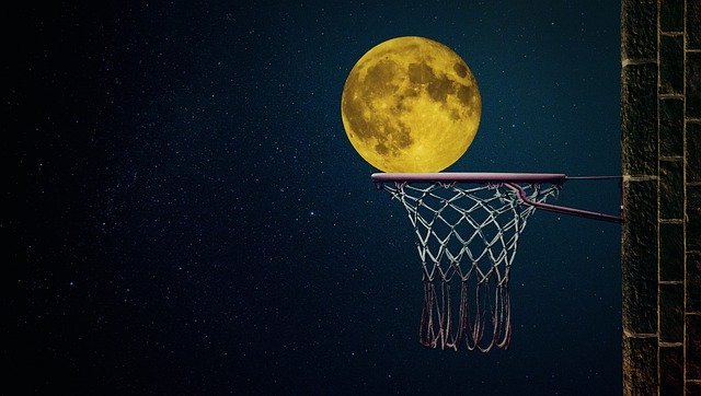A full moon perched on an outside basketball net.
