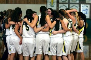 girls wearing white basketball uniforms arm-in-arm in huddle