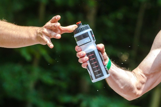 One hand reaching for a water bottle, another hand holding it out