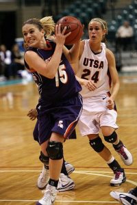 two women basketball players jostling closely on the court, front one holding a basketball up