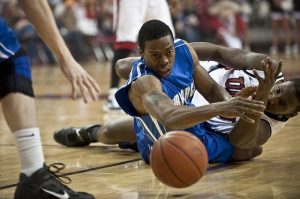 two basketball players scrambling on the floor of the court after a basketball