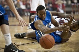 two basketball players scrambling on the floor of the court after a basketball