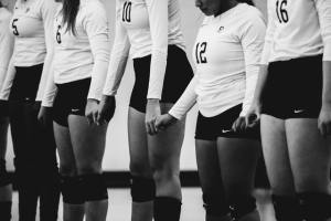 Team of girls wearing white long-sleeved tops, black shorts, Standing in a line on a court holding hands with heads bowed