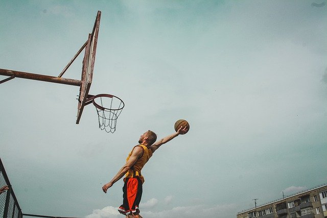 man flying through the air with a basketball in one hand ready to dunk in an outdoor basketball hoop