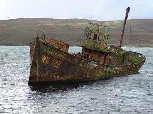 An old weather-worn skeleton of a ship sits in the water listing to the side.