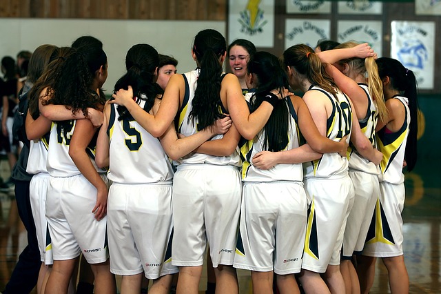 A women's basketball team in white uniforms huddled arm in arm on the court