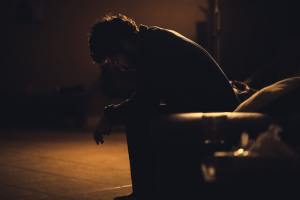 Shadow of a person sitting in a chair leaning forward with his arms resting on his thighs