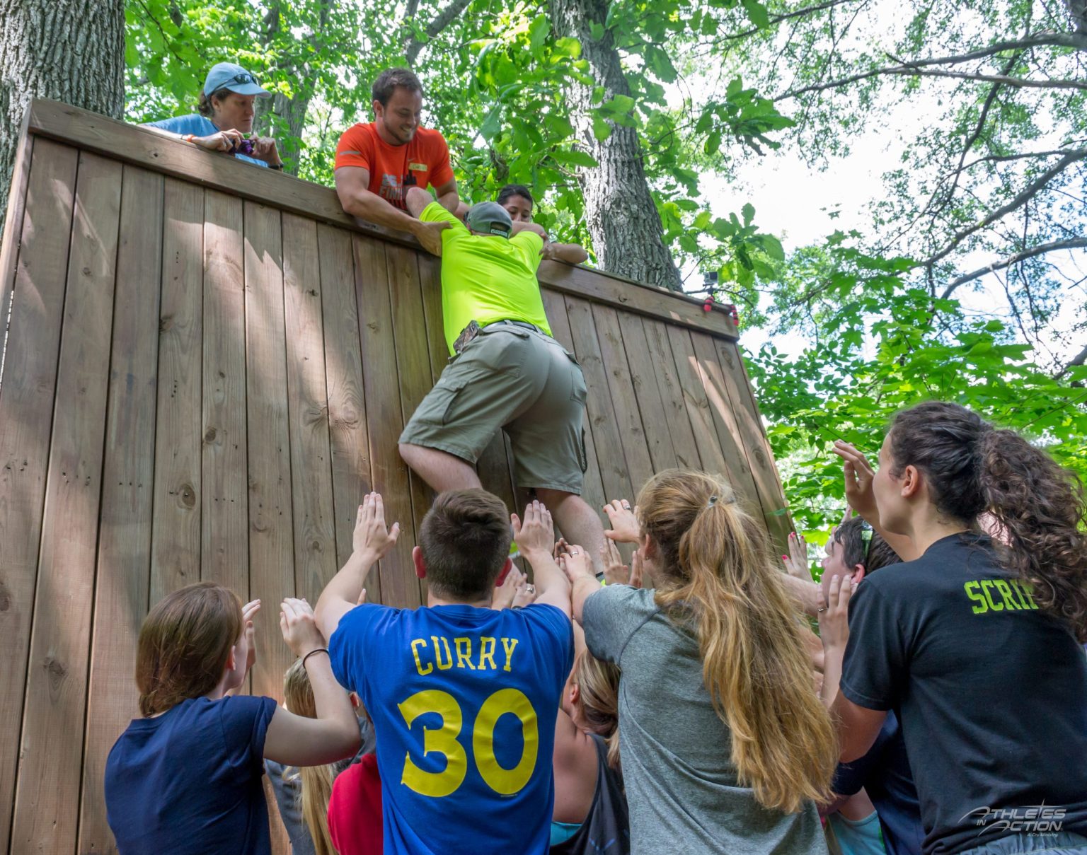 Teammates helping each other climb a wooden wall during a team-building challenge
