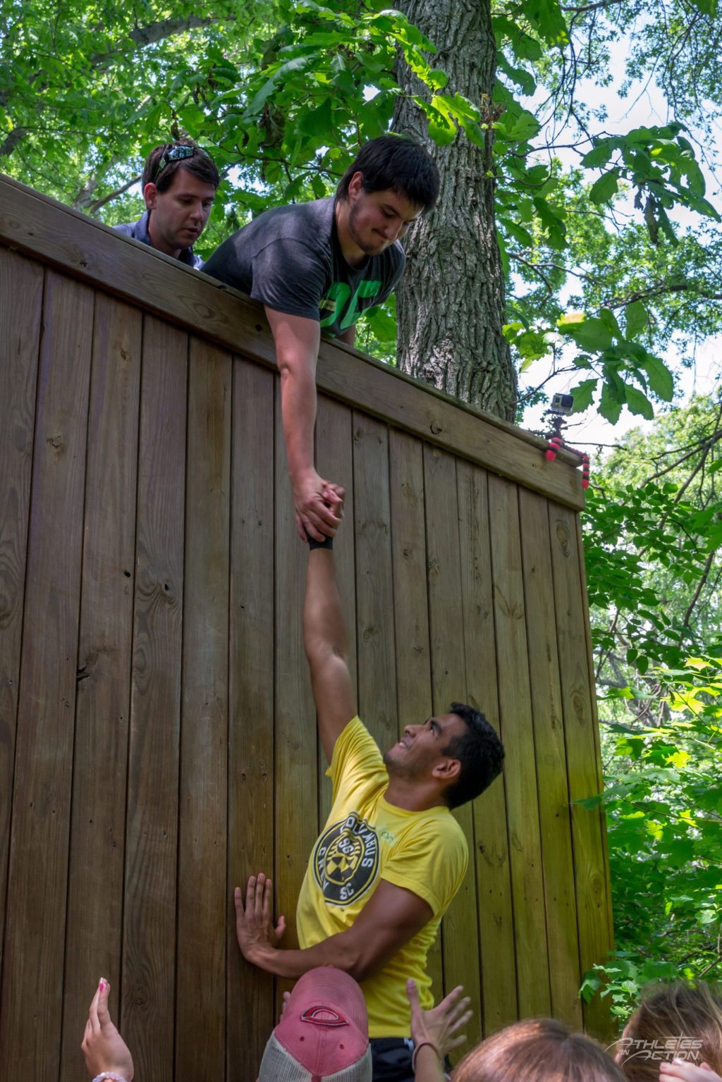 Athlete reaching down to pull a teammate up a climbing wall