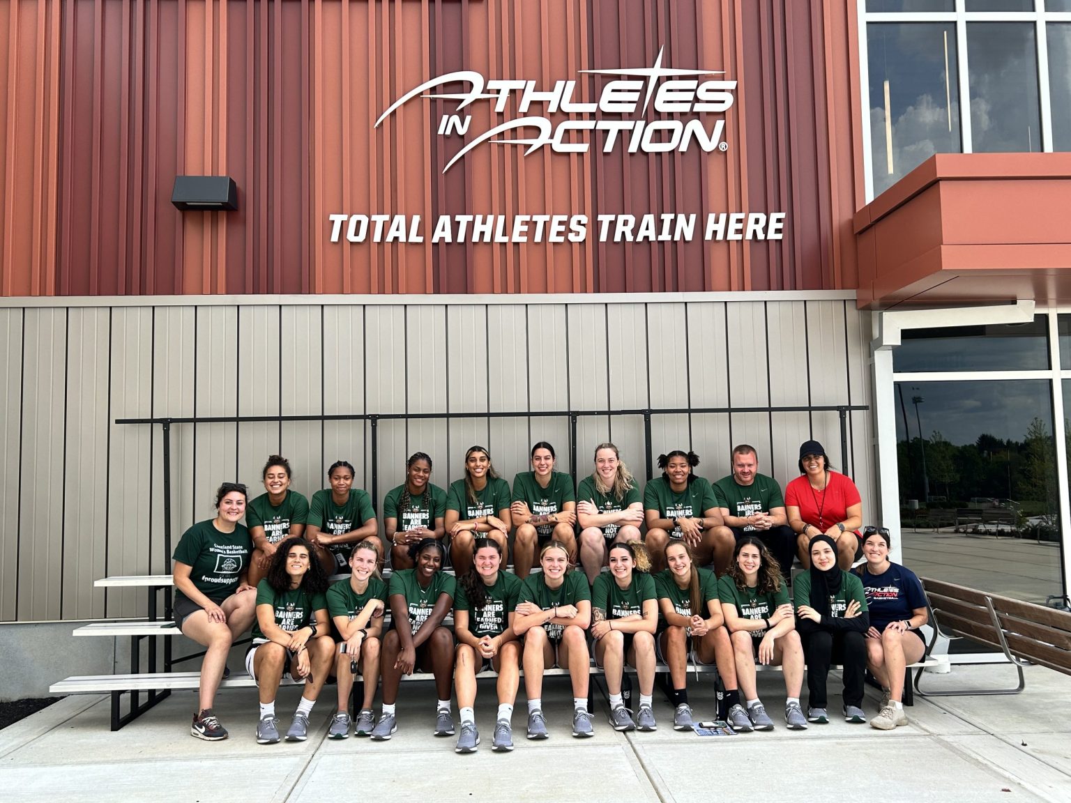 College team in green posing outside the Athletes in Action Fieldhouse