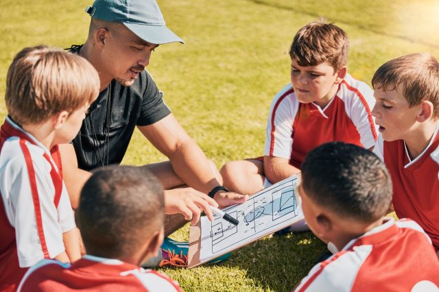 Tactics, children and soccer with a coach and team talking strategy before a game on an outdoor fie.