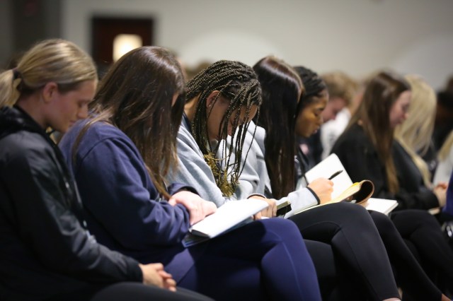 College athletes reading and taking notes in their Bibles at a retreat
