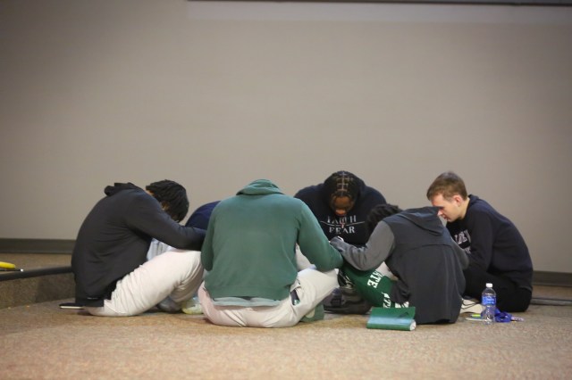 College athletes sitting in a circle on the floor, praying together at a retreat