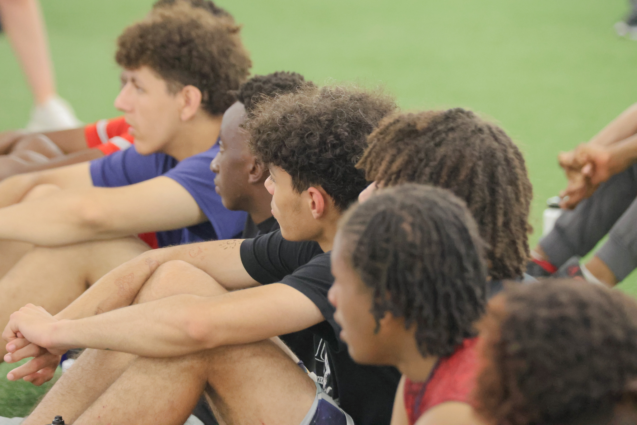 High school athletes sitting together on the turf, listening during an AIA camp session