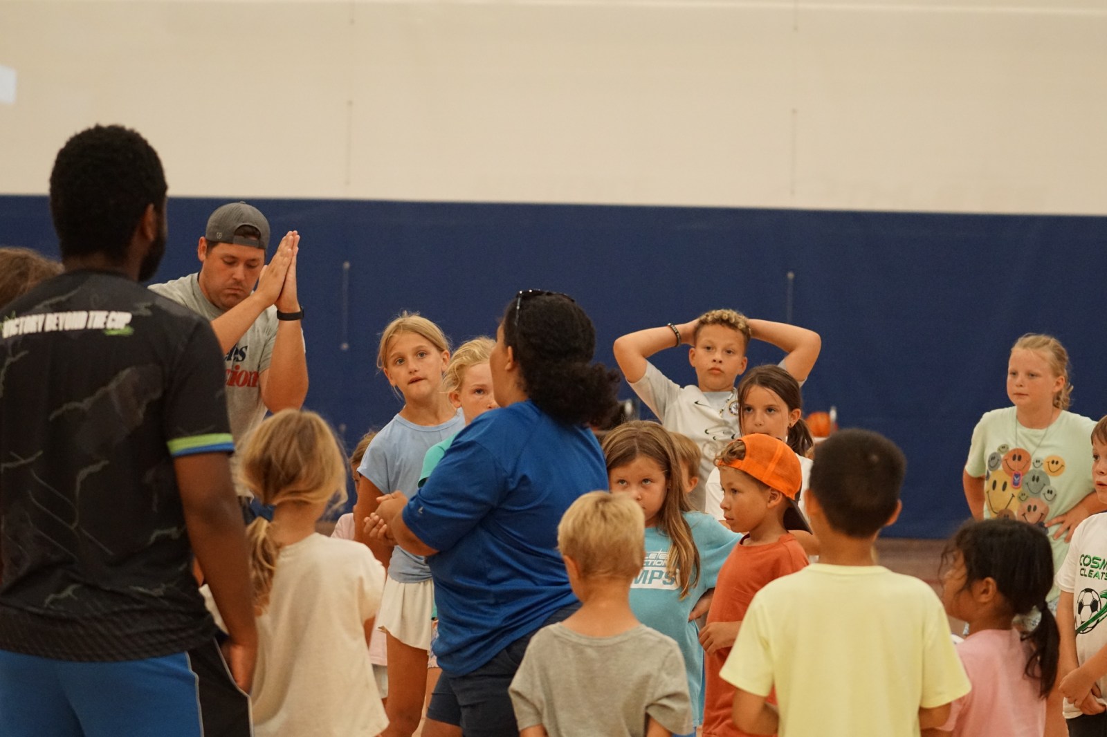 An AIA camp coach leading a group of young campers in the gym