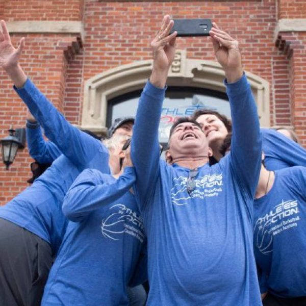 Several people in blue basketball shirts looking up at a phone, taking a selfie.